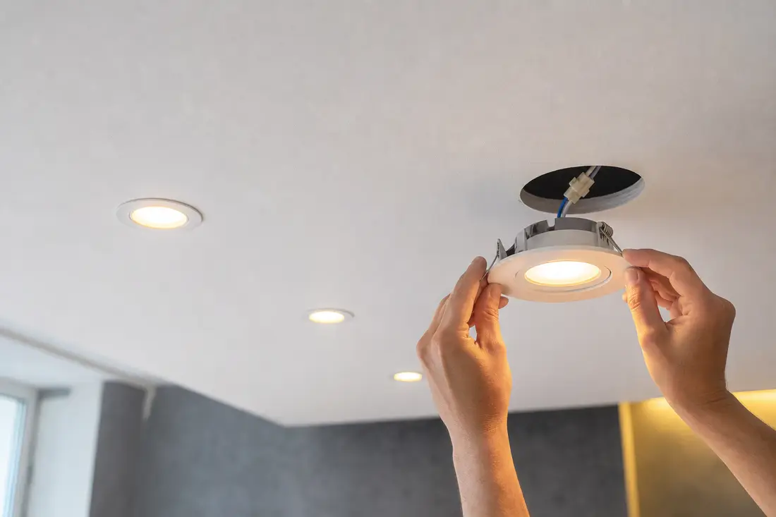 Électricien installant des spots LED encastrés dans un plafond lors d'une rénovation d'éclairage