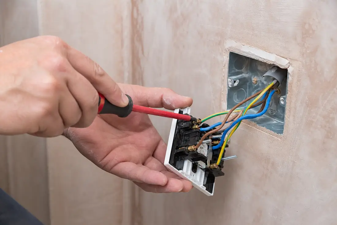 Électricien installant une nouvelle prise encastrée dans un mur lors d'une rénovation en Suisse romande